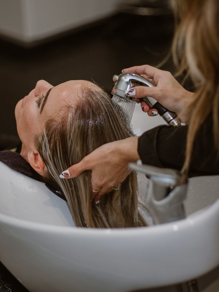 Hairdresser washing a client’s hair at the basin